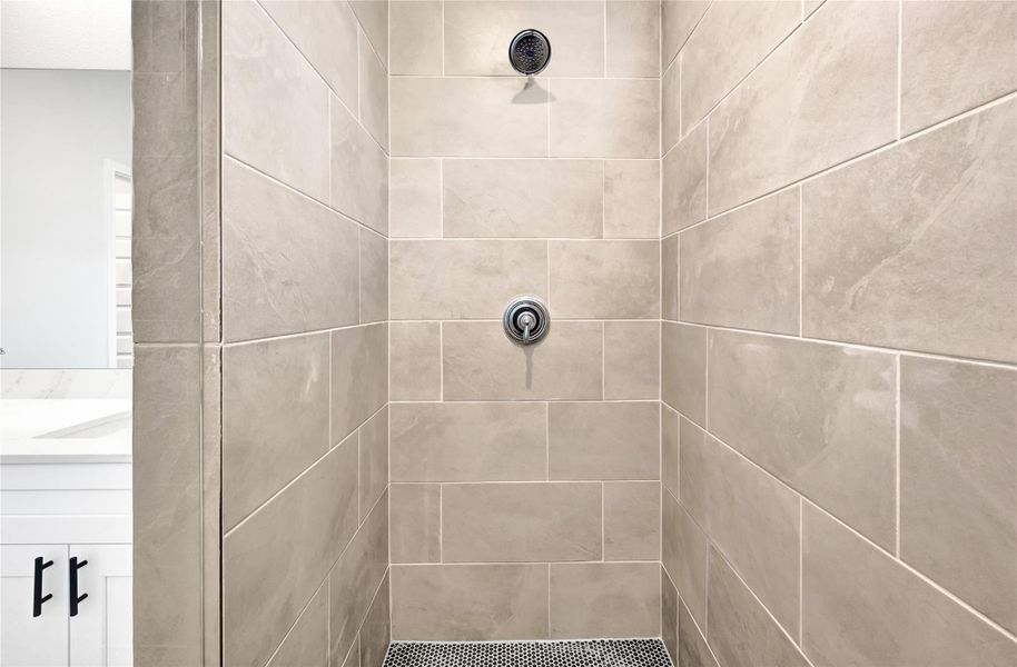 This photo showcases a modern shower with large, neutral-toned tiles and a sleek showerhead. The space has a clean and contemporary design, perfect for a stylish bathroom. Please note: The image is not the actual home; it is a home with the same floor plan in the neighborhood.
