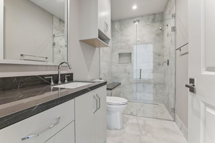 Luxury en-suite guest bath with custom built-ins, glass enclosed walk in shower and elegant quartz counter-top