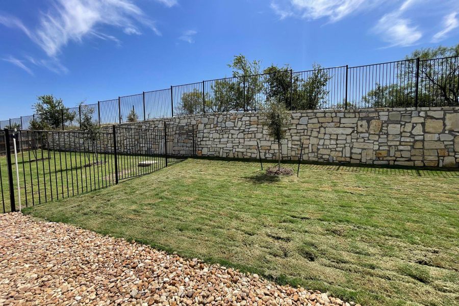 Stone retaining walls and secure fencing frame a manicured lawn under open skies. Stone retaining walls and secure fencing frame a manicured lawn under open skies.
