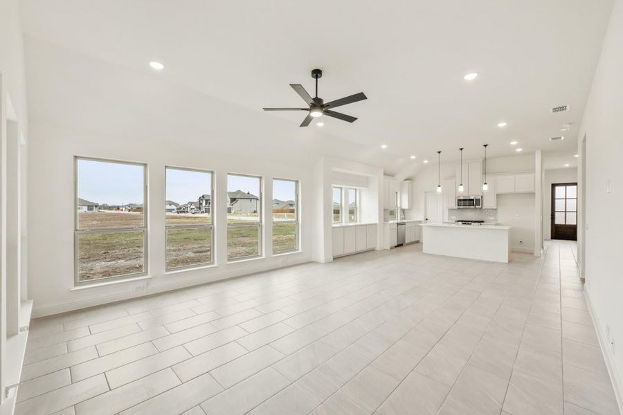 Open-concept living area with ceiling fan, tile floors, and white kitchen with island and pendant lights