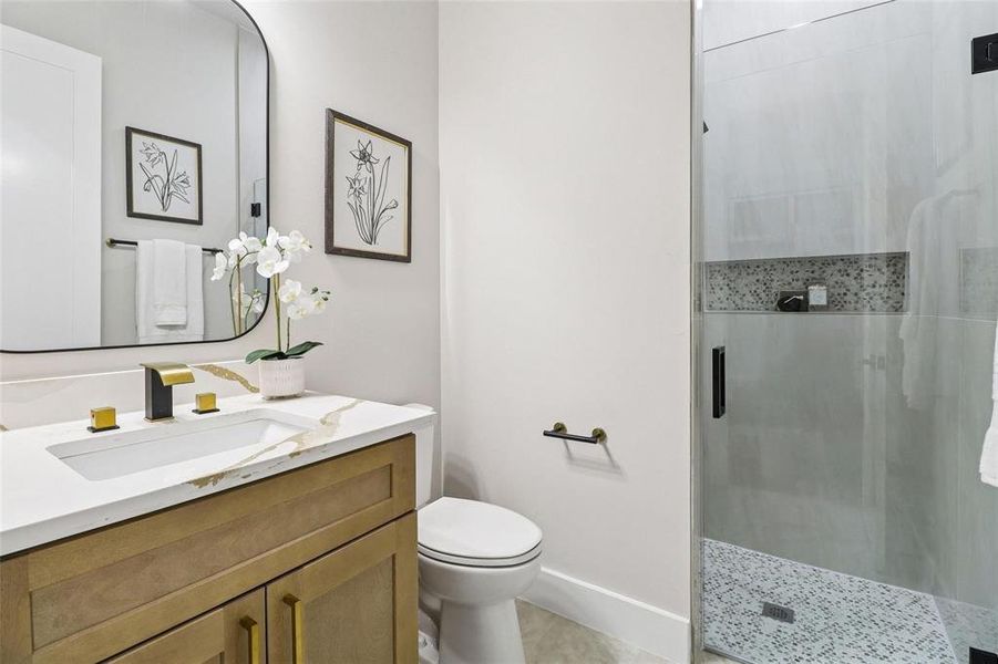 Bathroom featuring a glass-enclosed shower with mosaic tile floor, vanity with stone countertop, and black and gold fixtures
