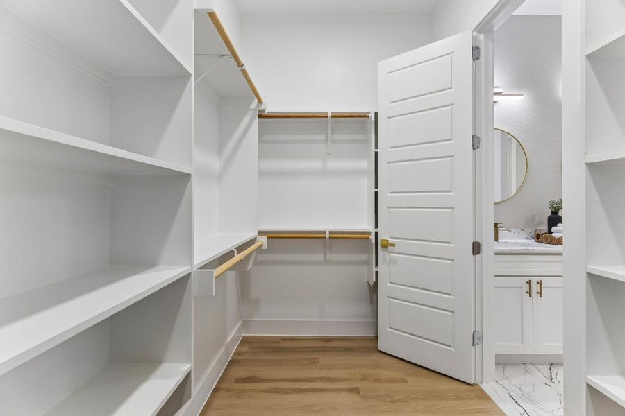 Ample shelving and hanging space defines this organized primary walk-in closet, with an adjoining well-appointed bathroom.