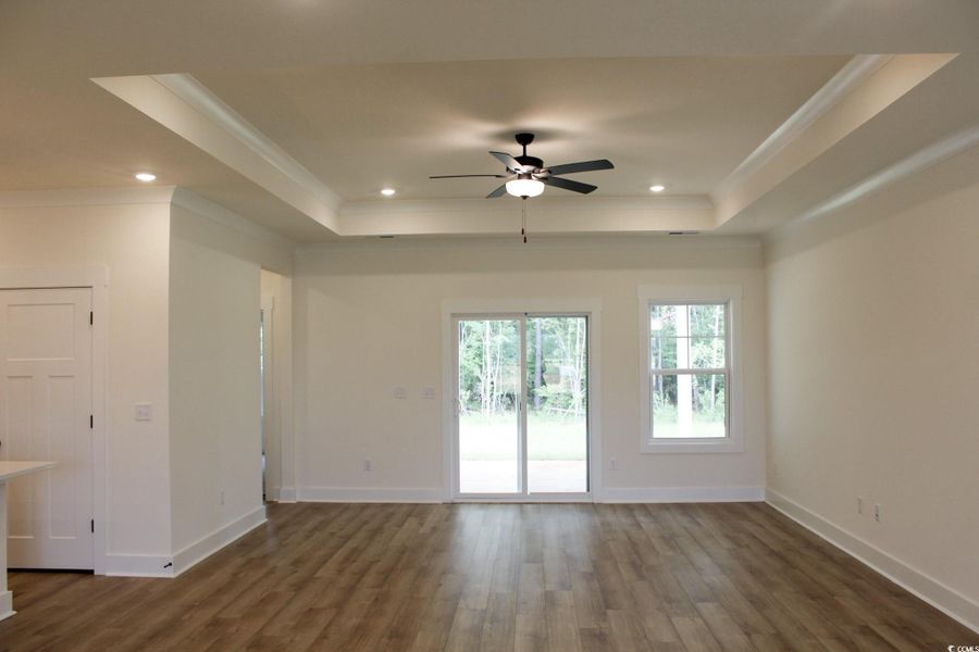 Unfurnished living room featuring dark wood finished floors, a raised ceiling, recessed lighting, ceiling fan, and ornamental molding