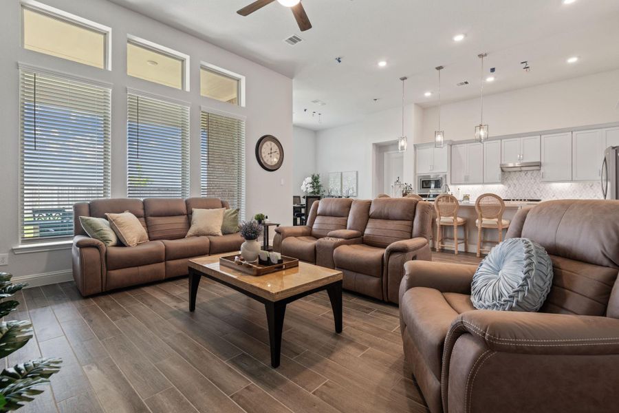 This spacious, open-concept living area features comfortable brown leather seating, large windows with ample natural light, and a view of the modern kitchen with white cabinetry and pendant lighting. The space is perfect for entertaining and relaxation. This spacious, open-concept living area features comfortable brown leather seating, large windows with ample natural light, and a view of the modern kitchen with white cabinetry and pendant lighting. The space is perfect for entertaining and relaxation.