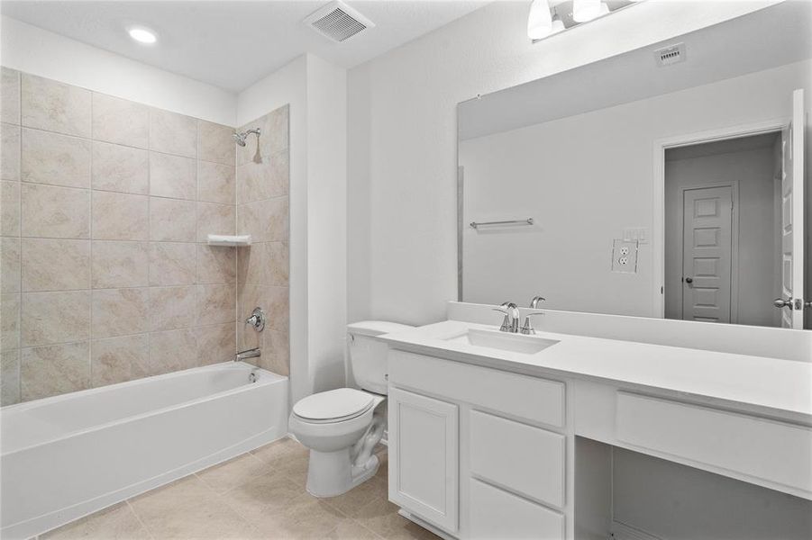 Secondary bath features tile flooring, bath/shower combo with tile surround, wood cabinets, beautiful light countertops, mirror, sleek fixtures and modern finishes.