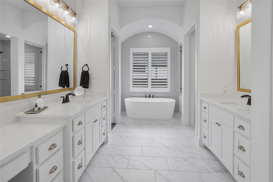 Spacious bath featuring dual vanities with white cabinetry and stone countertops