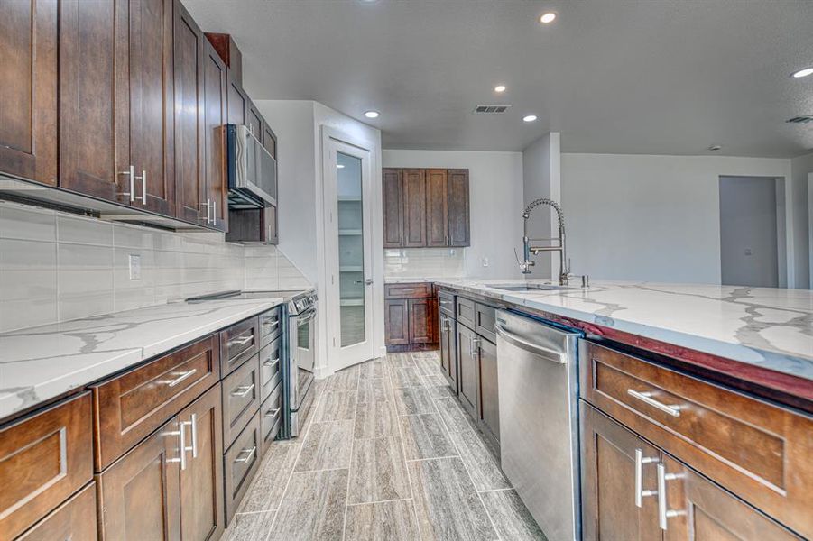 Kitchen featuring tasteful backsplash, light stone countertops, sink, light hardwood / wood-style floors, and stainless steel appliances