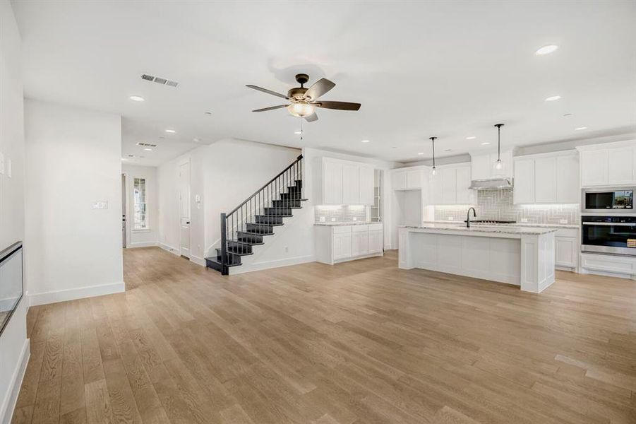 Open-concept living space featuring wood-finish flooring, a contemporary kitchen, a staircase with dark banisters, recessed lighting, and a ceiling fan