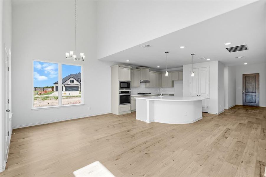 Kitchen with open floor plan, an island with sink, light wood-style floors, appliances with stainless steel finishes, and a chandelier Kitchen with open floor plan, an island with sink, light wood-style floors, appliances with stainless steel finishes, and a chandelier
