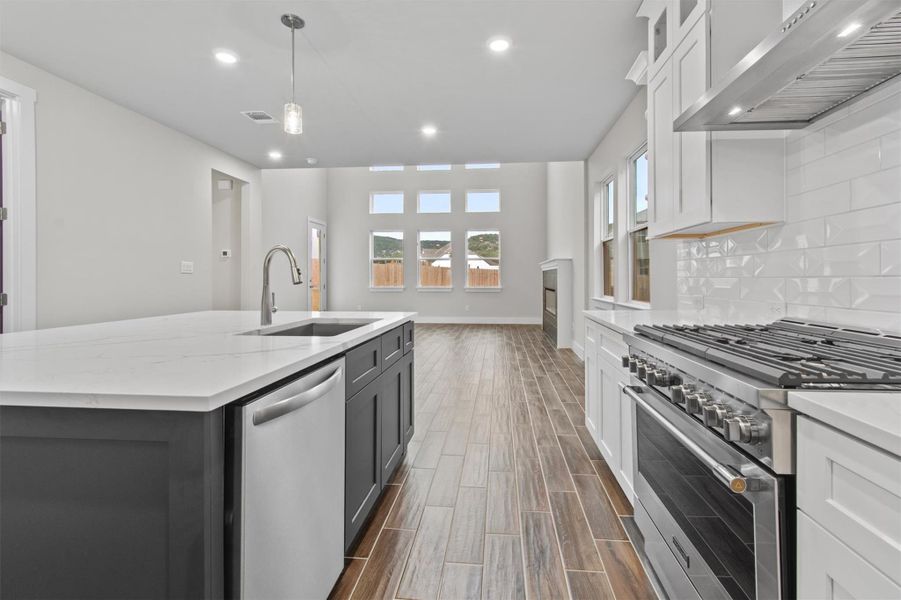 Kitchen with white cabinetry, an island with sink, appliances with stainless steel finishes, wall chimney range hood, and sink