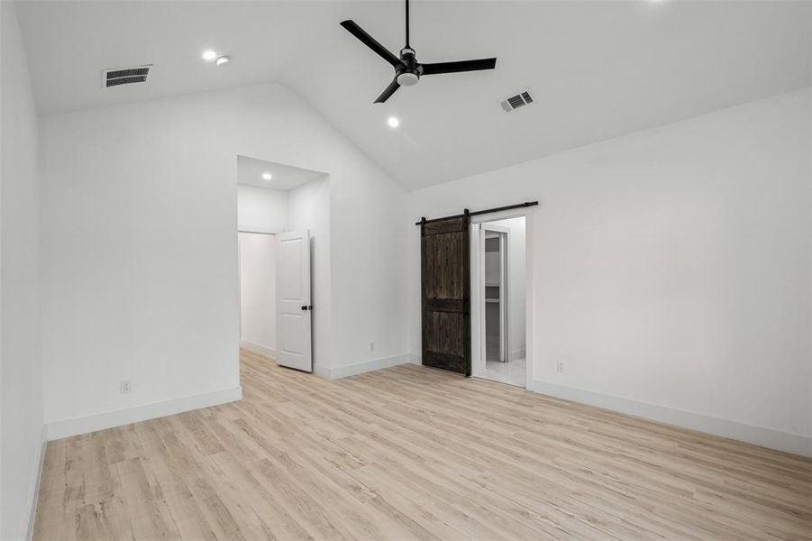 Unfurnished room featuring a barn door, ceiling fan, light hardwood / wood-style floors, and vaulted ceiling