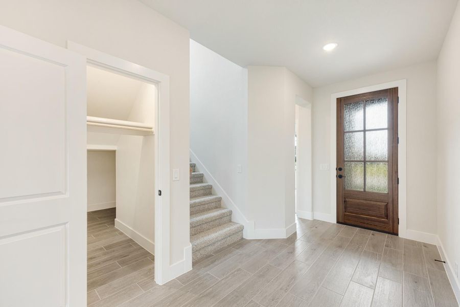 Entryway with wood front door, carpeted staircase, and light wood-look tile floors next to an open closet.