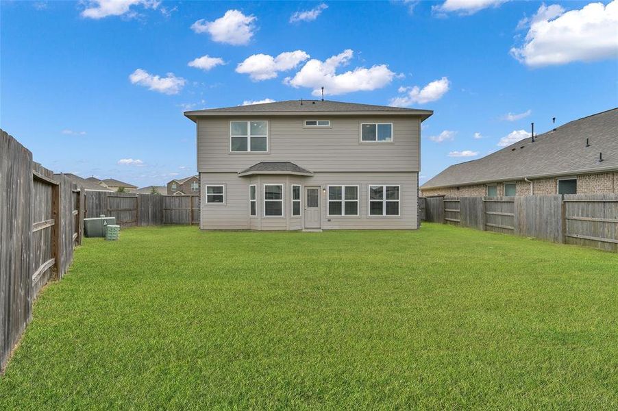 This image shows the rear exterior of a two-story home with a sizable, fenced backyard. The house features a neutral color palette and multiple windows for natural light.