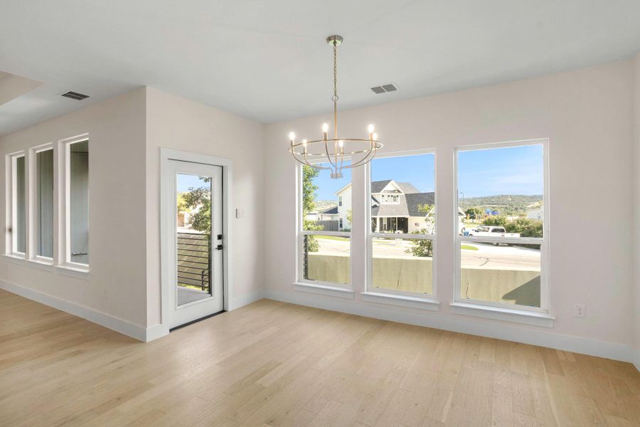 Spacious room featuring light wood-finish flooring, a contemporary chandelier, multiple large windows, and a glass-paneled door leading to an exterior balcony with metal railings Spacious room featuring light wood-finish flooring, a contemporary chandelier, multiple large windows, and a glass-paneled door leading to an exterior balcony with metal railings