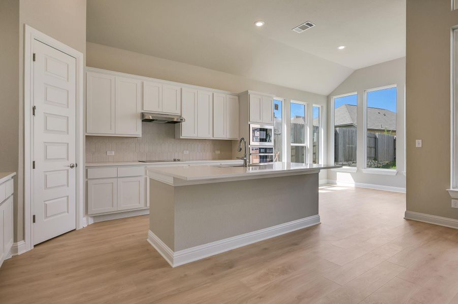 Kitchen with decorative backsplash, white cabinetry, a kitchen island with sink, light wood-style flooring, and recessed lighting
