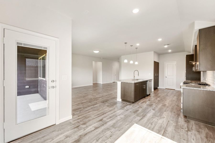 Open-concept kitchen and living area with dark cabinets, center island, pendant lights, and light wood floors