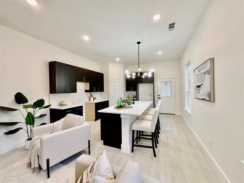 Kitchen with a kitchen breakfast bar, hanging lights, tasteful backsplash, a center island with sink, and light wood-type flooring