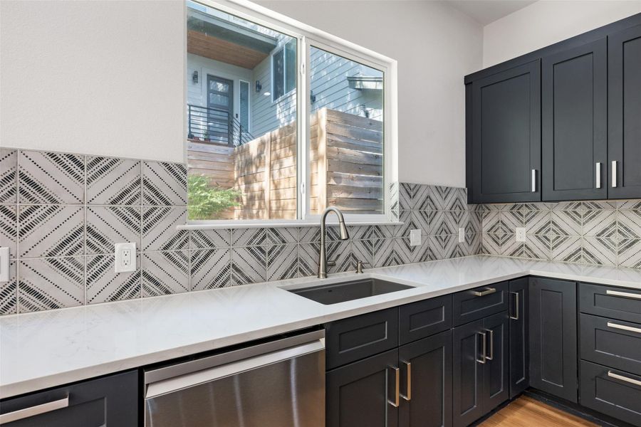 Kitchen featuring dishwasher, light stone counters, healthy amount of natural light, and tasteful backsplash