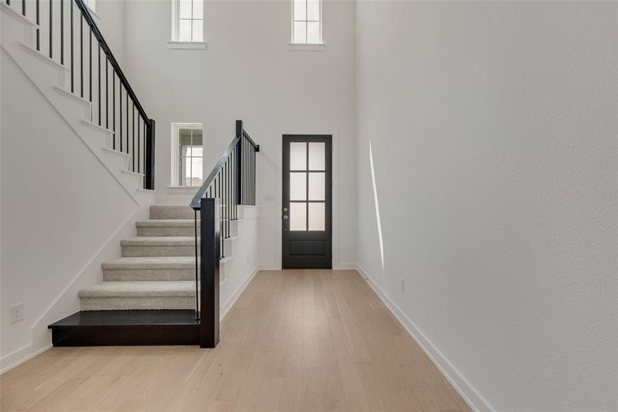 Foyer with plenty of natural light, stairs, light wood-type flooring, and a towering ceiling Foyer with plenty of natural light, stairs, light wood-type flooring, and a towering ceiling