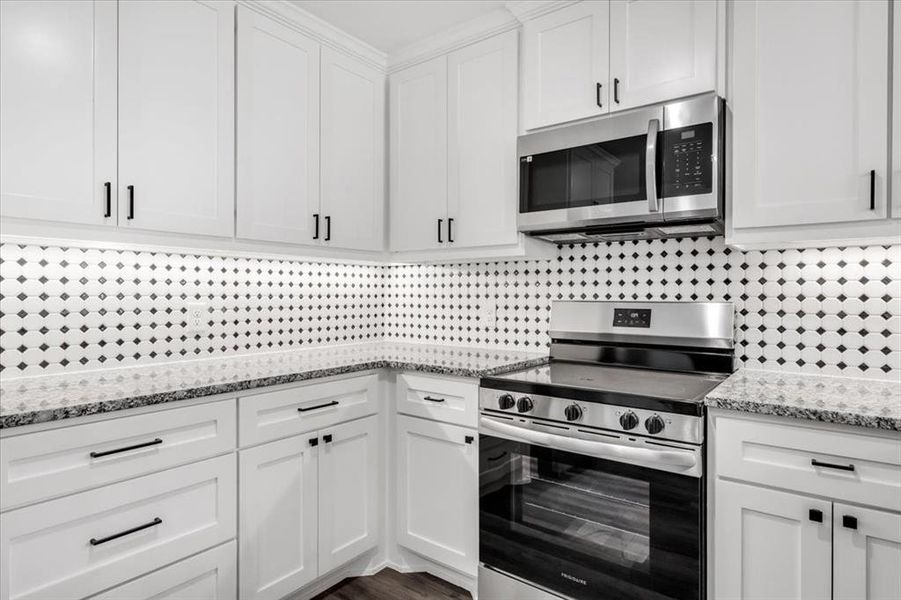 Kitchen featuring backsplash, white cabinetry, light stone counters, and stainless steel appliances