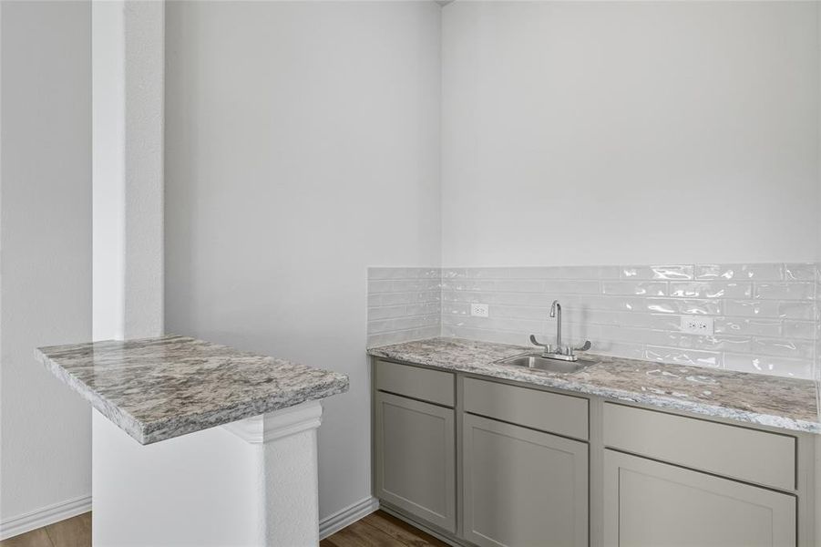 Bar area with gray cabinets, light wood-style flooring, light stone countertops, and backsplash Bar area with gray cabinets, light wood-style flooring, light stone countertops, and backsplash