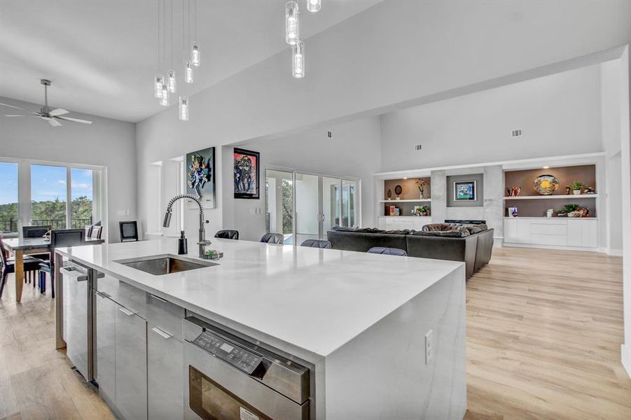 Kitchen featuring built in shelves, decorative light fixtures, an island with sink, open floor plan, and light wood-style floors