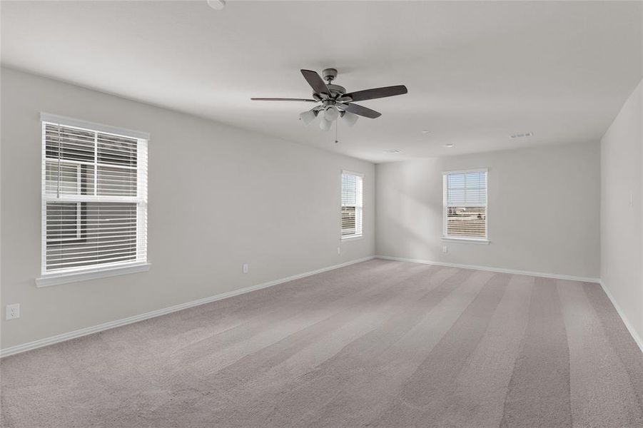 This spacious primary bedroom features neutral walls, carpeted flooring, and abundant natural light from several windows. Very expansive with plenty of space to customize.