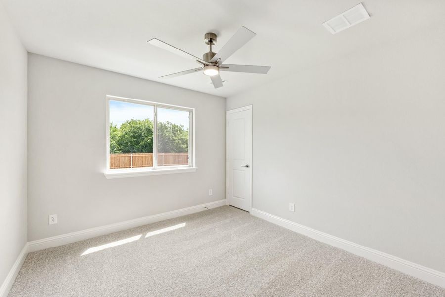 Empty bedroom with carpet flooring, ceiling fan, and a window overlooking a fenced backyard Empty bedroom with carpet flooring, ceiling fan, and a window overlooking a fenced backyard