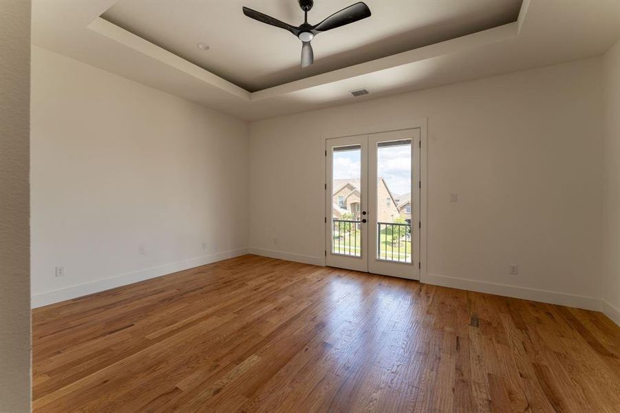 Empty room featuring a tray ceiling, light wood finished floors, a ceiling fan, and french doors