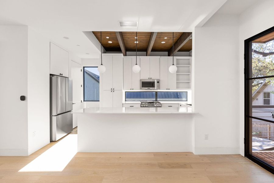 Kitchen featuring a peninsula, stainless steel appliances, white cabinets, light wood-style floors, and decorative light fixtures