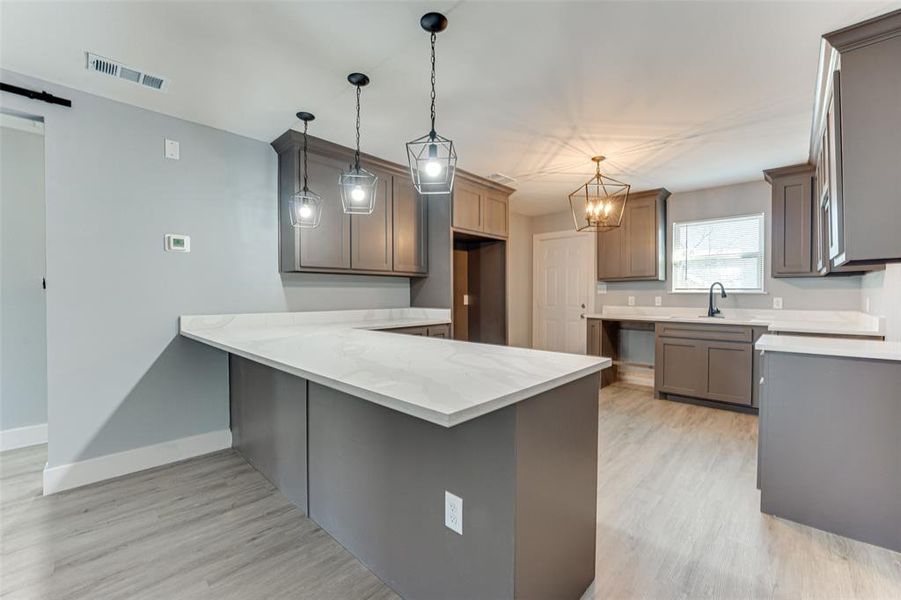 Kitchen featuring a barn door, decorative light fixtures, kitchen peninsula, and light wood-type flooring