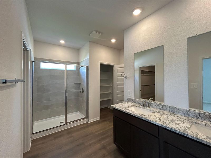 Full bathroom with a spacious closet, a textured wall, dark wood-type flooring, double vanity, and a stall shower