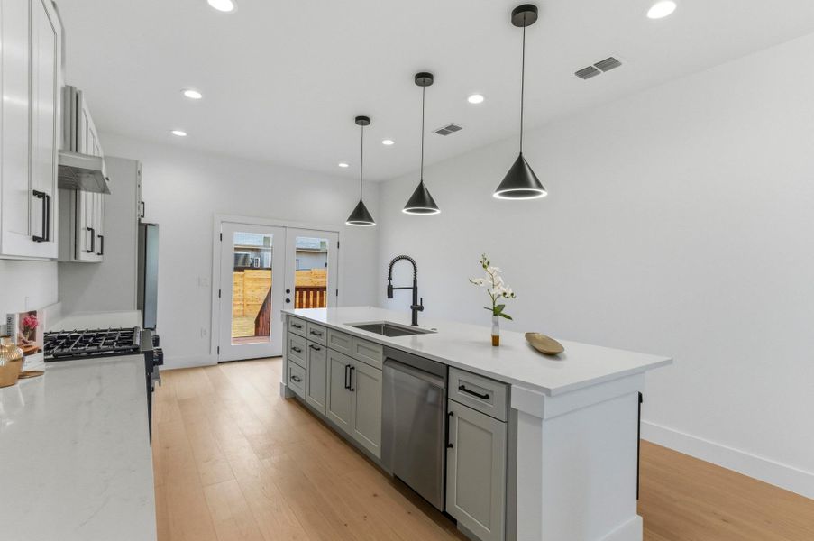 Kitchen featuring decorative light fixtures, gray cabinetry, an island with sink, light stone countertops, and stainless steel appliances