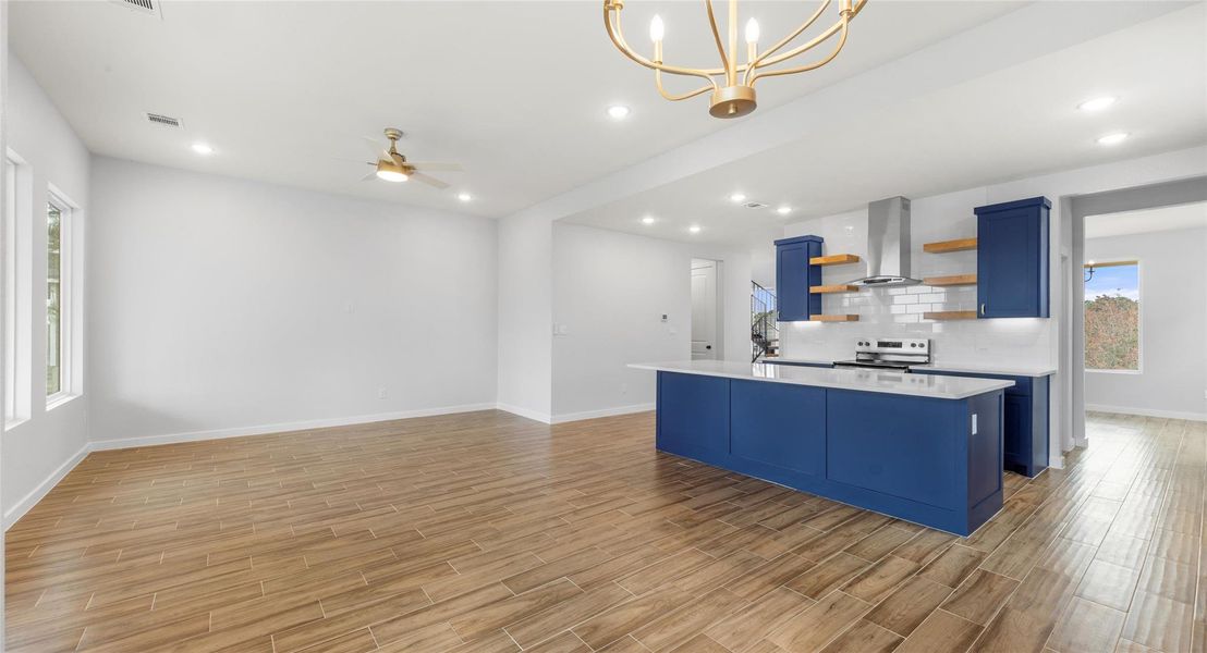 Kitchen with blue cabinetry, open shelves, a center island with sink, ceiling fan, and open floor plan