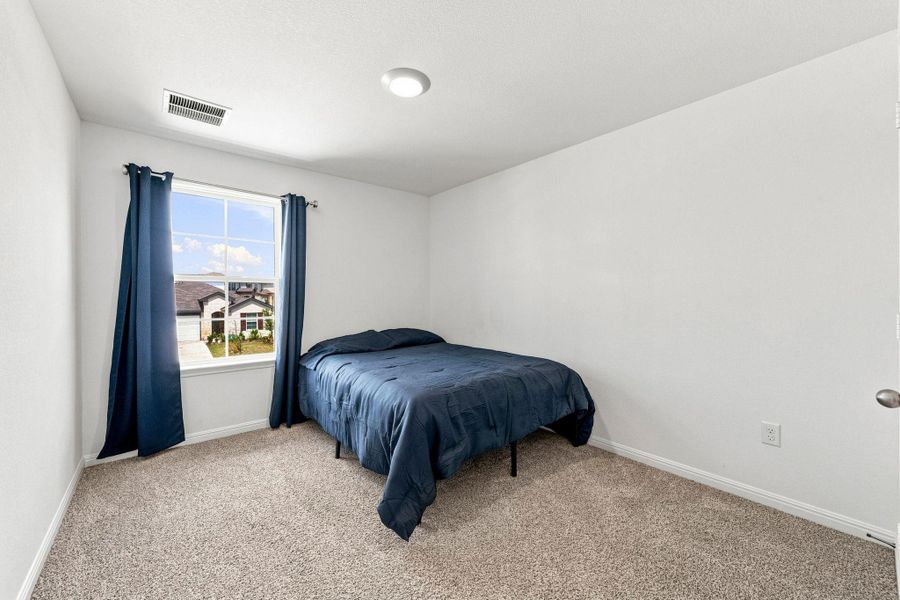 Natural light pours through a multi-pane window in this carpeted bedroom.