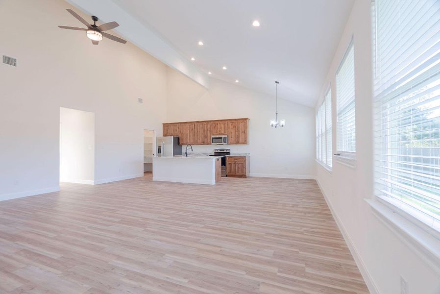 Unfurnished living room with light wood-style floors, beam ceiling, high vaulted ceiling, a chandelier, and ceiling fan Unfurnished living room with light wood-style floors, beam ceiling, high vaulted ceiling, a chandelier, and ceiling fan