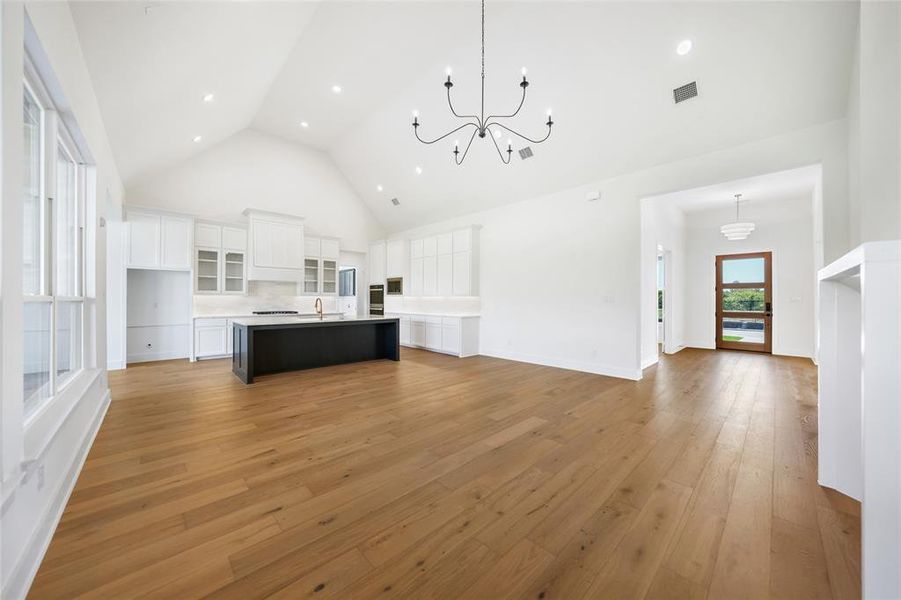 Kitchen with open floor plan, white cabinets, a chandelier, high vaulted ceiling, and glass insert cabinets