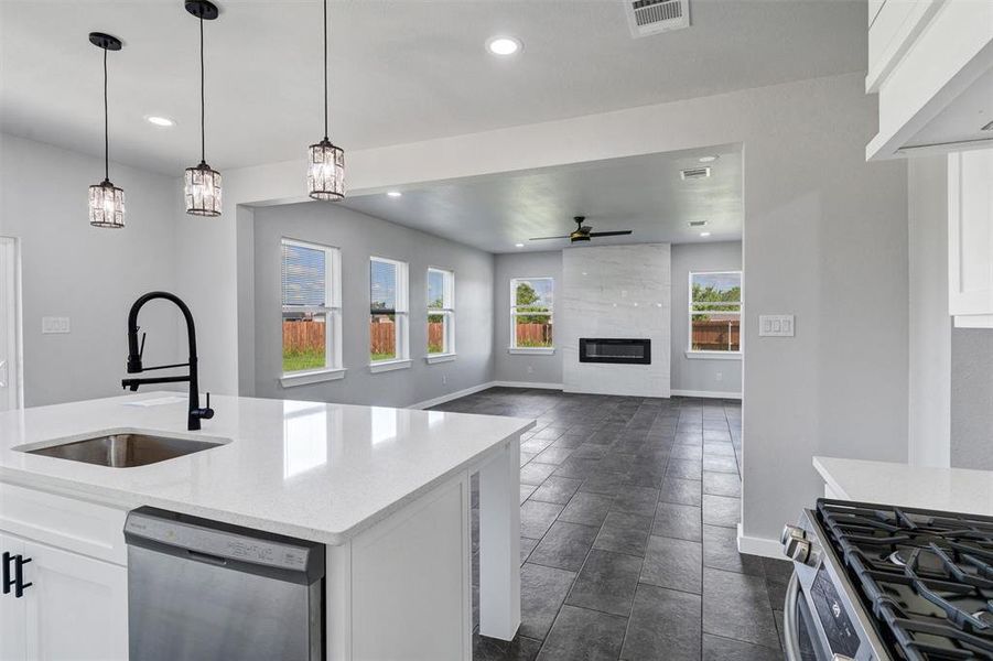 Kitchen featuring stainless steel appliances, a sink, baseboards, ceiling fan, and a tile fireplace