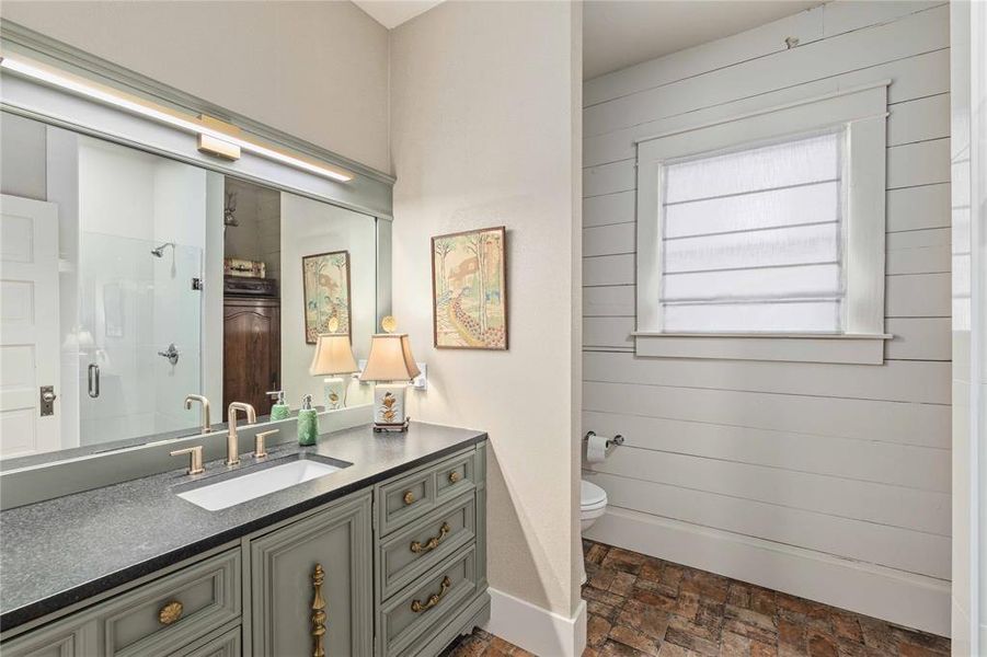 Bathroom vanity featuring a dark countertop, undermount sink, and brass-finish fixtures