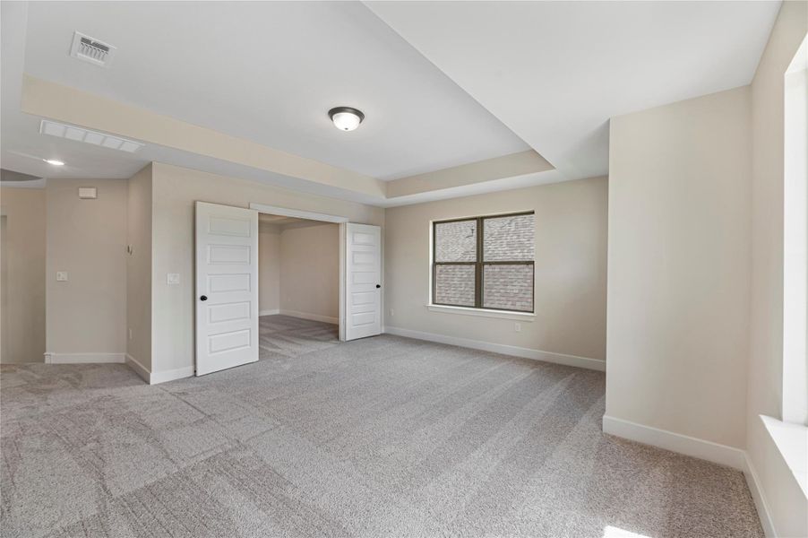 Unfurnished bedroom with light colored carpet and a tray ceiling