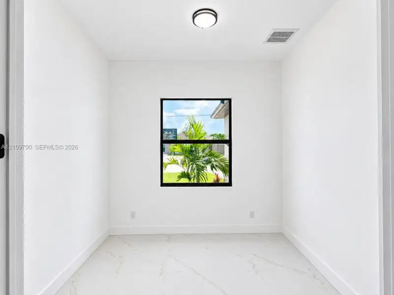 Neutral interior room featuring white walls, large-format tile flooring with veining, and a window with a black frame