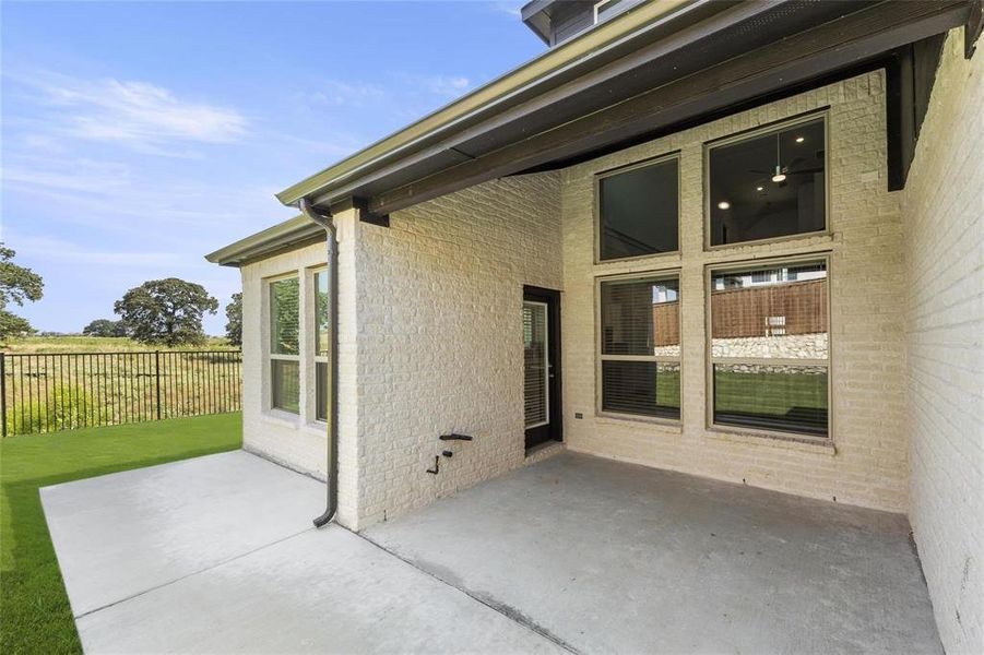 Expansive covered patio featuring a concrete surface, white brick exterior, and a series of large windows Expansive covered patio featuring a concrete surface, white brick exterior, and a series of large windows