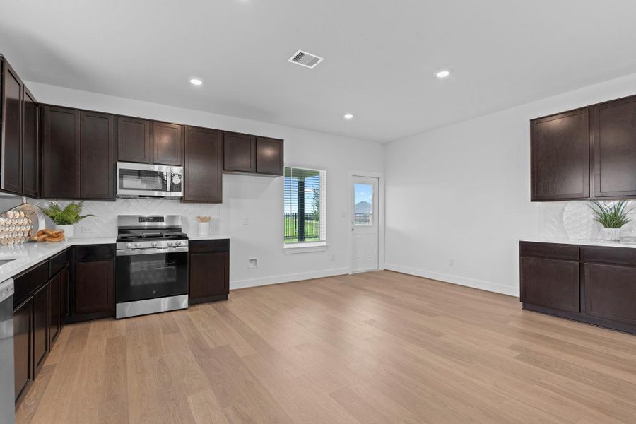Another wide-angle view of the kitchen reveals a generous layout, dark cabinetry, quartz countertops, and woodlike vinyl flooring—designed for both beauty and function in everyday living. **Image Representative of Plan Only and May Vary as Built**. Another wide-angle view of the kitchen reveals a generous layout, dark cabinetry, quartz countertops, and woodlike vinyl flooring—designed for both beauty and function in everyday living. **Image Representative of Plan Only and May Vary as Built**.