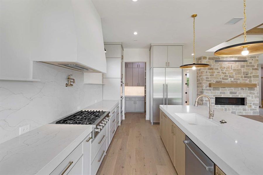 Kitchen with light stone counters, hanging light fixtures, light hardwood / wood-style flooring, backsplash, and stainless steel appliances