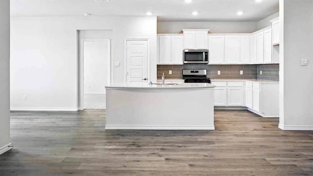 Modern kitchen featuring white cabinetry, stainless steel appliances, a grey subway tile backsplash, and a central island with an undermount sink