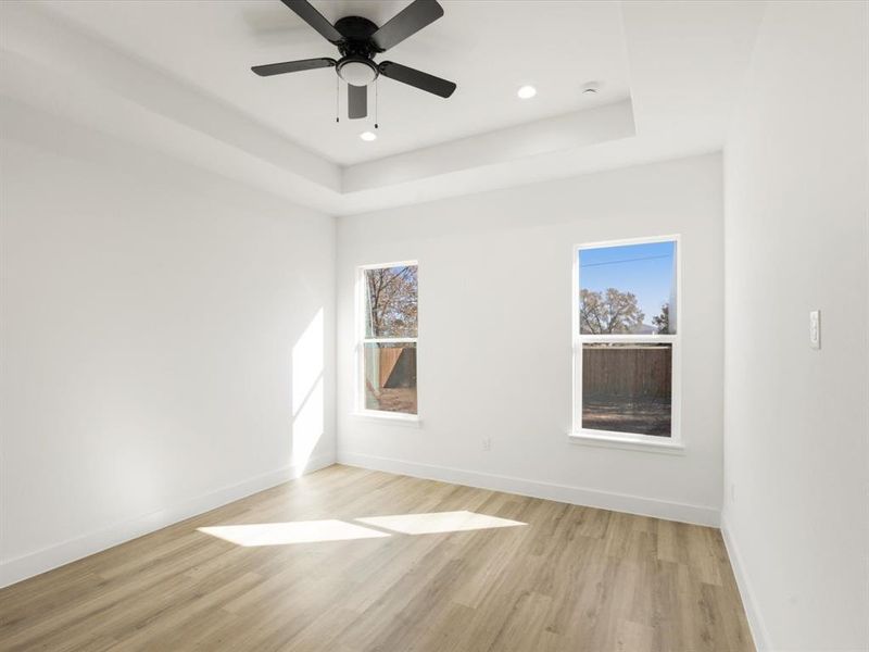Empty room with light wood finished floors, a raised ceiling, a ceiling fan, and recessed lighting