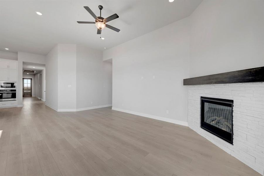 Unfurnished living room with a ceiling fan, recessed lighting, a fireplace, and light wood finished floors Unfurnished living room with a ceiling fan, recessed lighting, a fireplace, and light wood finished floors
