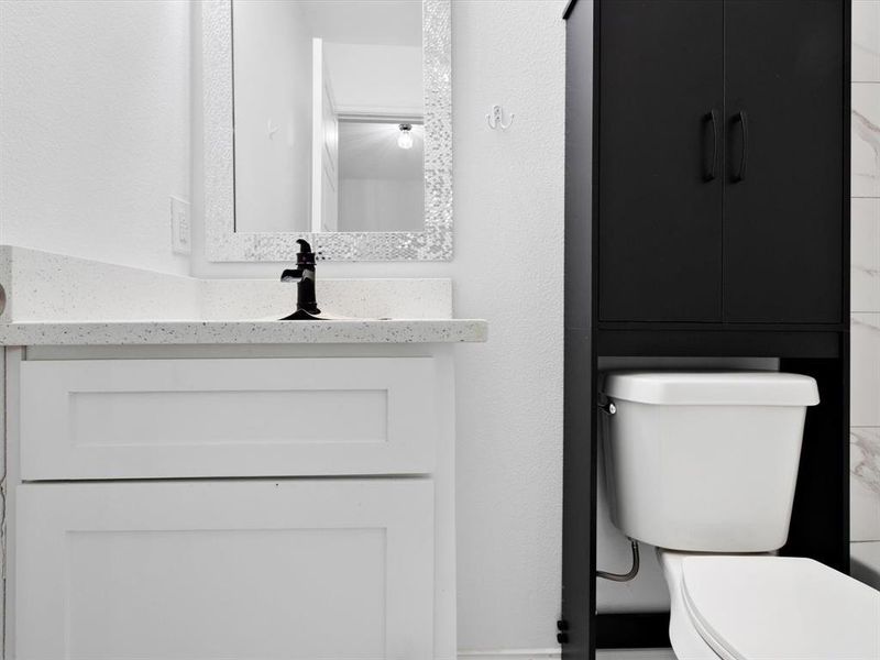 Bathroom featuring a white shaker-style vanity, black single-handle faucet, and a black over-the-toilet storage cabinet