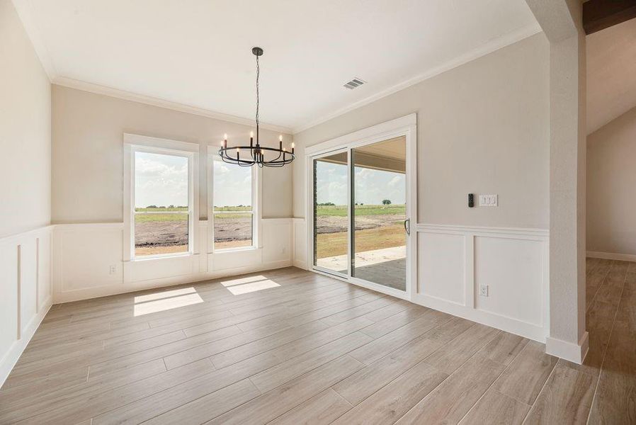 Unfurnished dining area with a chandelier, a wainscoted wall, ornamental molding, light wood-style floors, and a decorative wall Unfurnished dining area with a chandelier, a wainscoted wall, ornamental molding, light wood-style floors, and a decorative wall