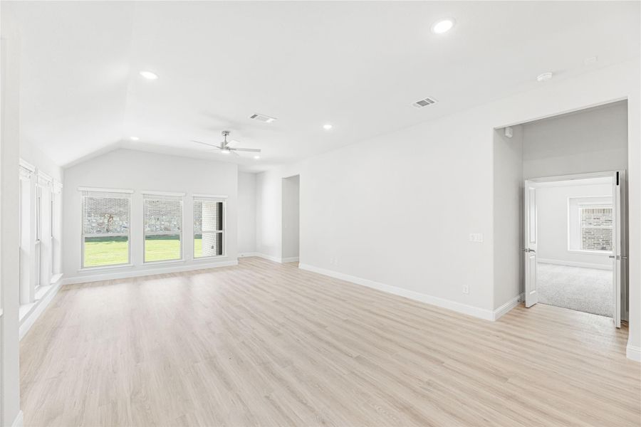 Open living room with vaulted ceiling, ceiling fan, light wood floors, and large windows Open living room with vaulted ceiling, ceiling fan, light wood floors, and large windows